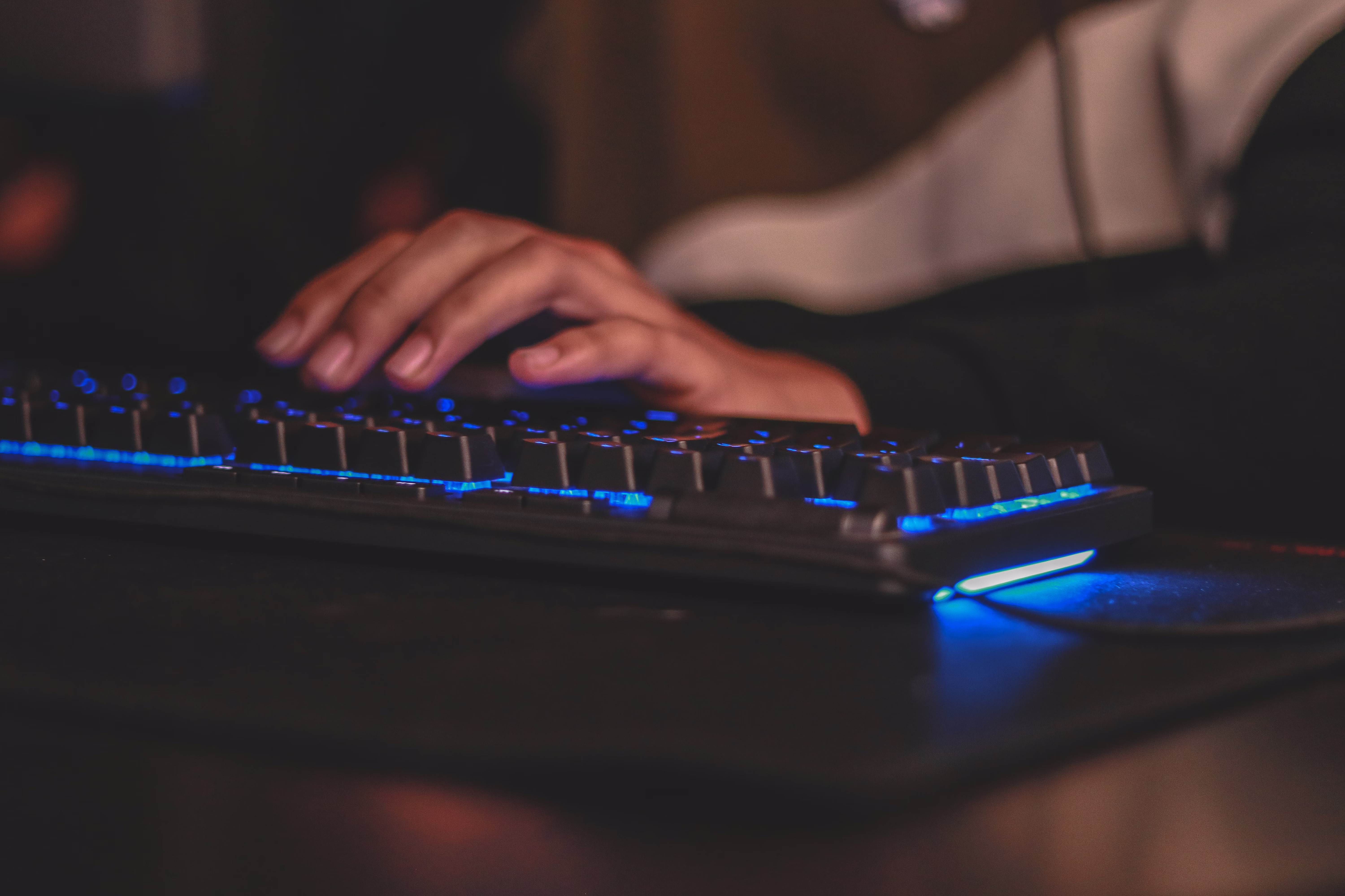 Close-up of hands typing on a sleek laptop illuminated by electric blue lighting.